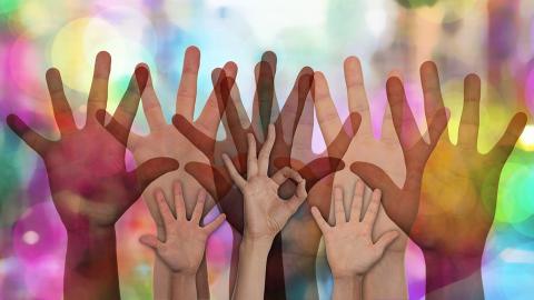 Multiple hands raised against multi-colour background