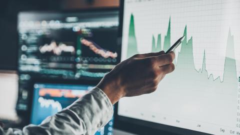 Hand holding a pen following the peaks and troughs of a graph on screen