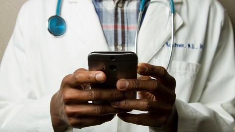 Doctor wearing a stethoscope and white lab coat holding a smartphone