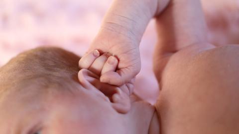 Newborn baby with hand against its ear