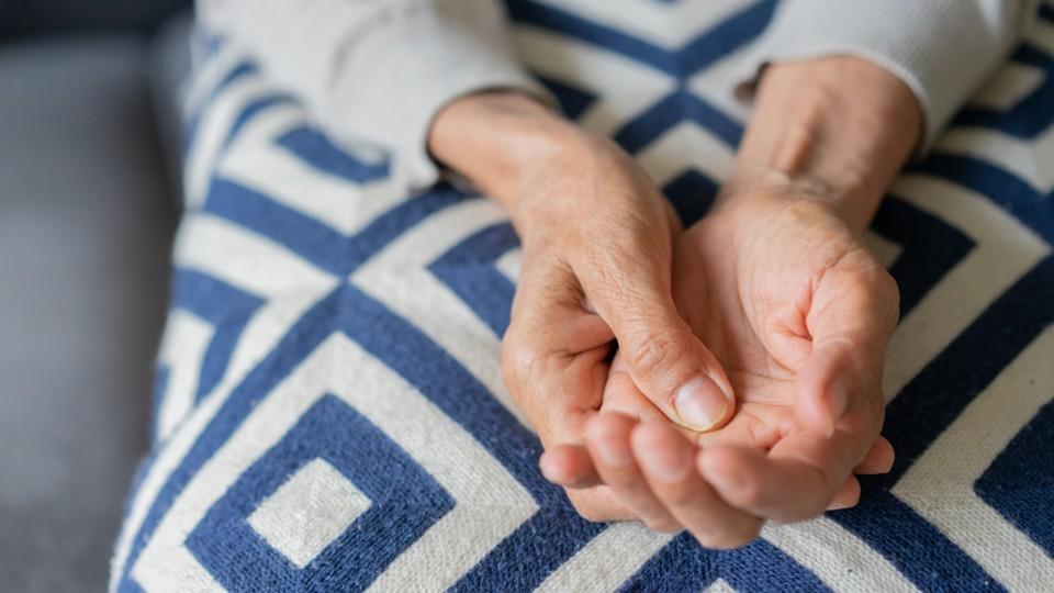 An elderly woman holds her hand to stop shaking
