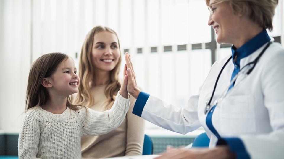 Young girl gives high five to her female doctor, mum also in the consult room