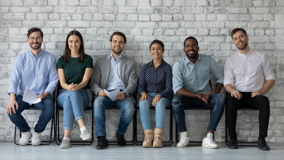 applicants for hiring process sit against a gray painted brick wall