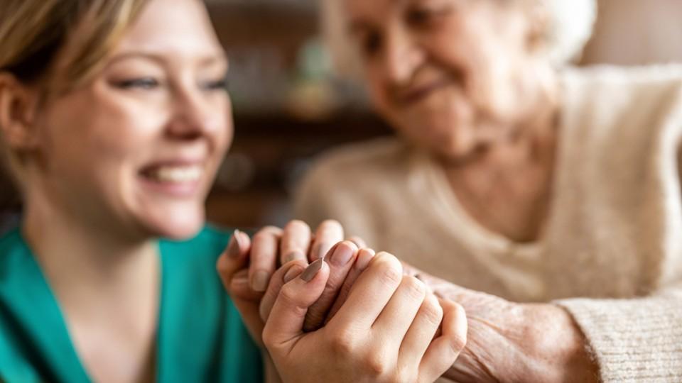 Middle aged female nurse holds hand of elderly woman
