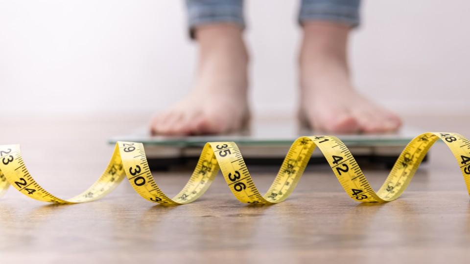person standing on scales behind a yellow measuring tape