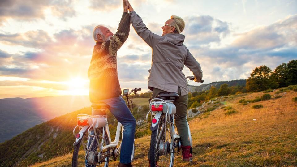 Older couple high five each other on bicycles at top of hill