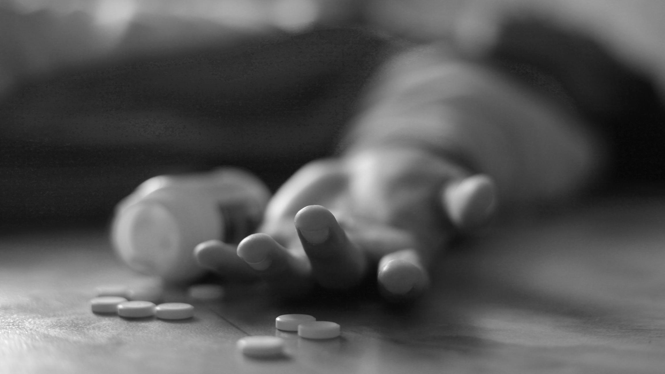 Man lies on floor next to spilled pill bottle, reference to overdose