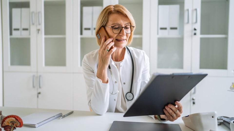 Female HCP in her office on phone holding clipboard of patient information