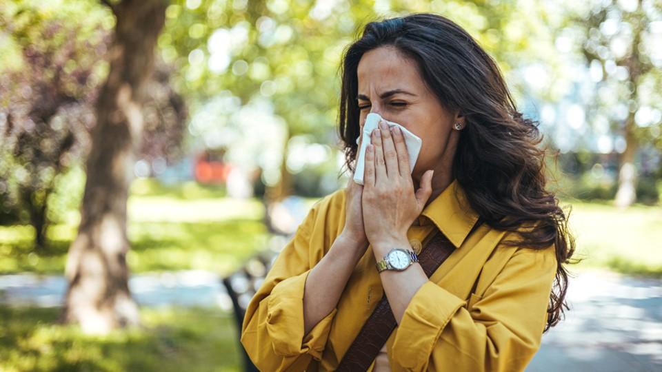 Woman in yellow jacket blows nose due to hayfever