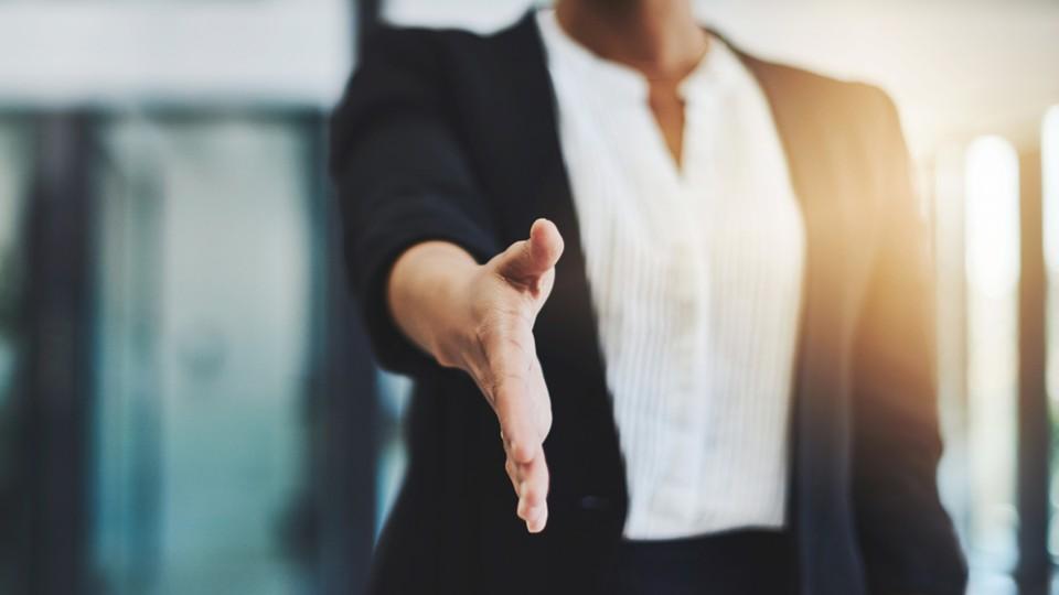 Woman in black suit extends hand of welcome to the company
