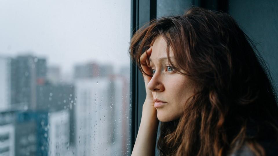 Depressed woman looks out rain spattered window in city