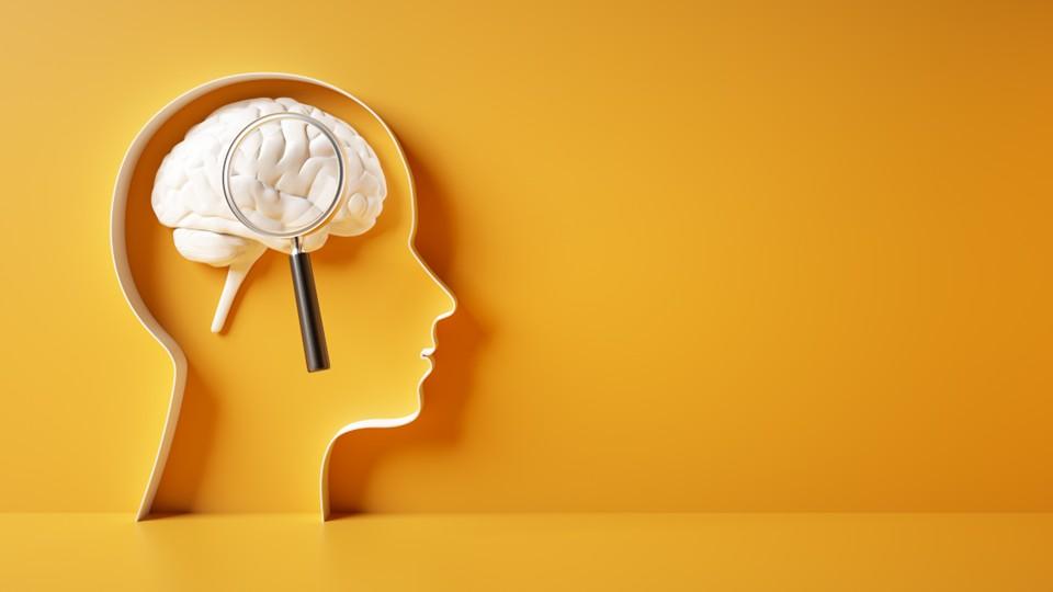 Silhouette of a head with white brain under magnifying glass inside outline, against yellow background
