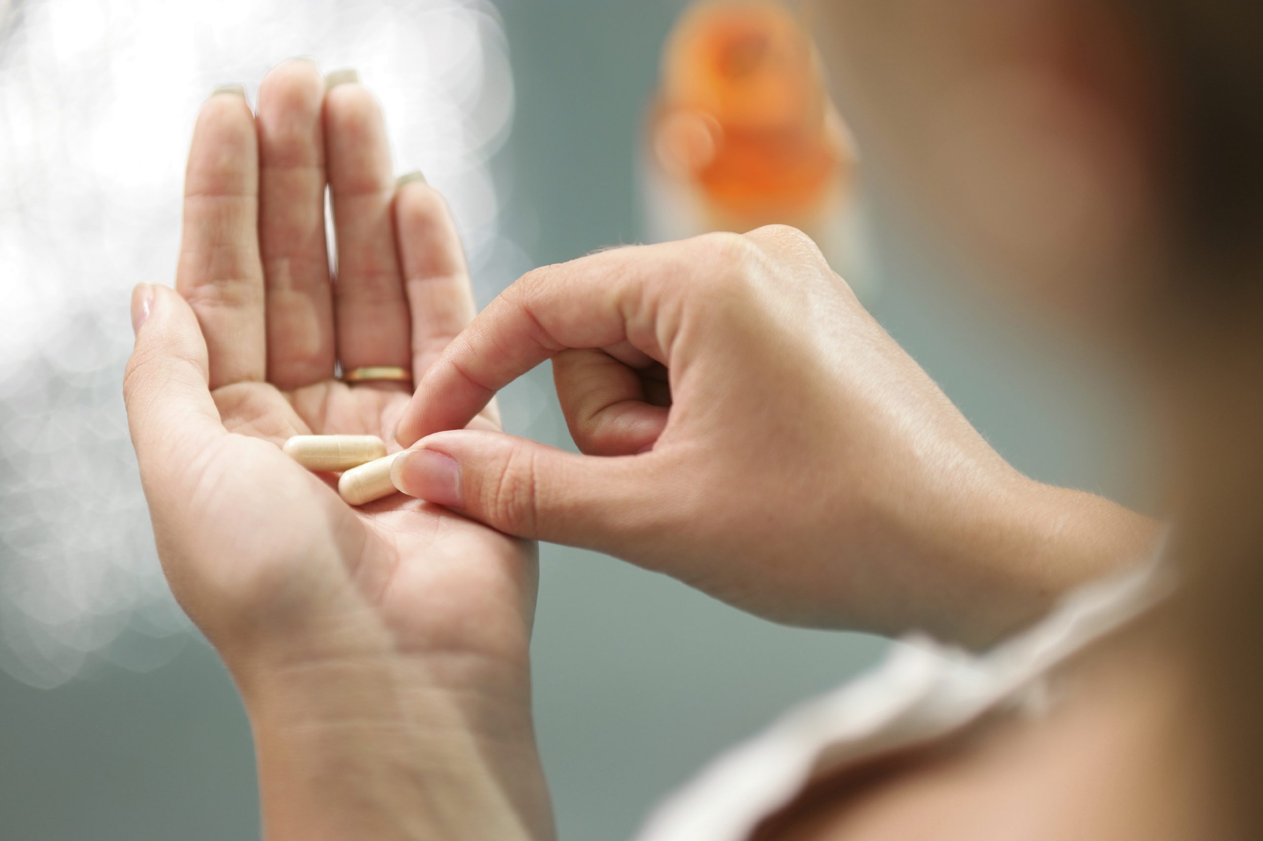 Close up view of young woman holding ginseng vitamins and minerals pills in hand with capsule bottle on table. High angle view