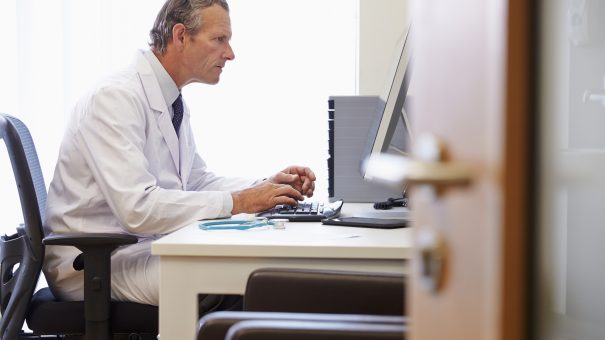 Male Doctor In Office Working At Computer