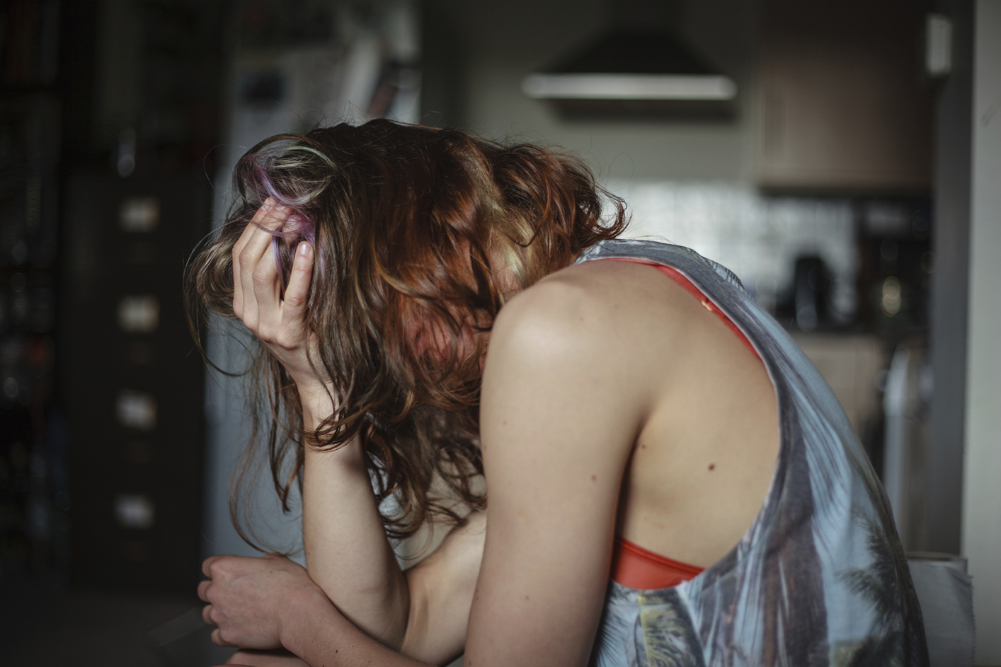 A sad young woman is sitting in her kitchen with a headache