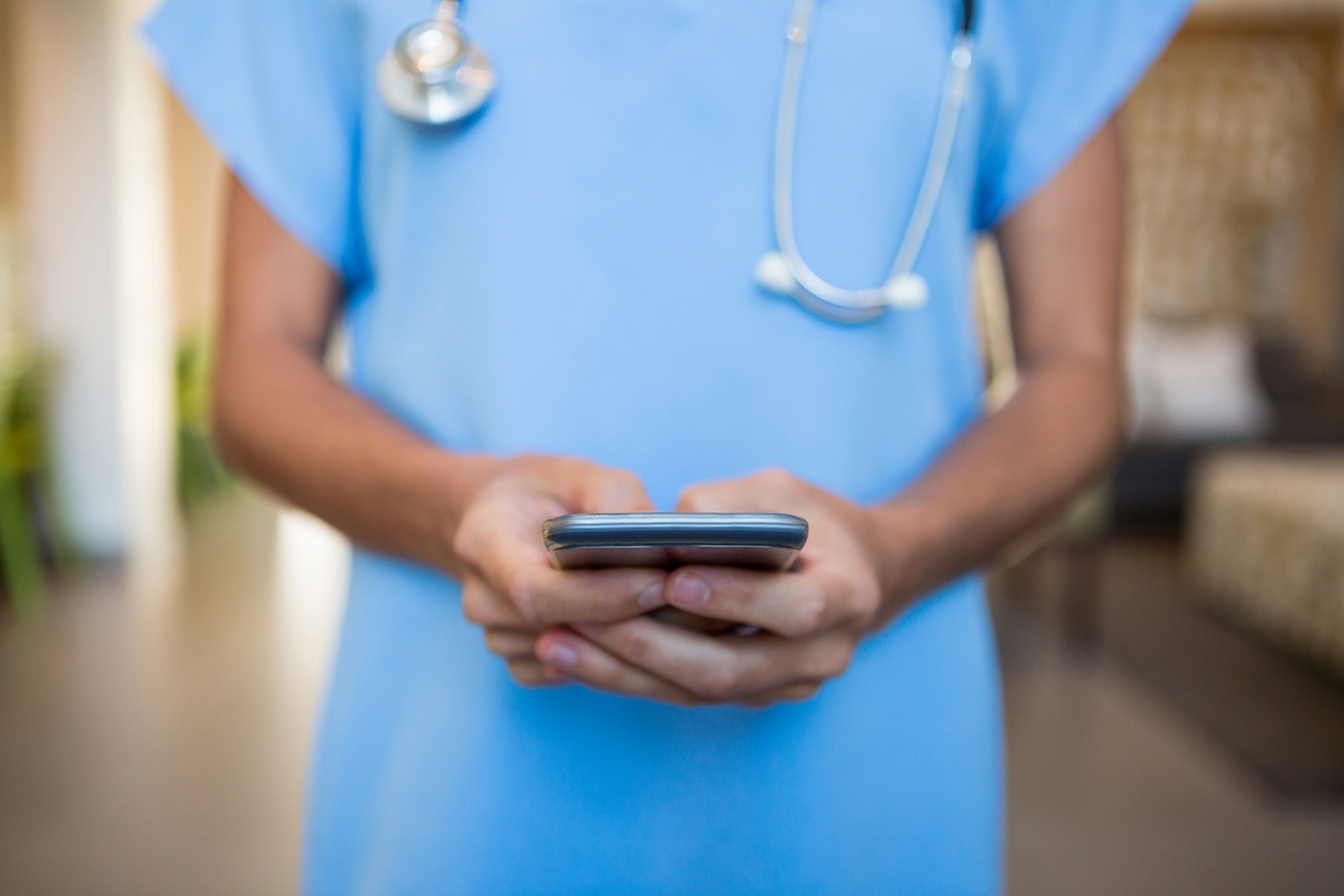 Mid-section of doctor using mobile phone in hospital