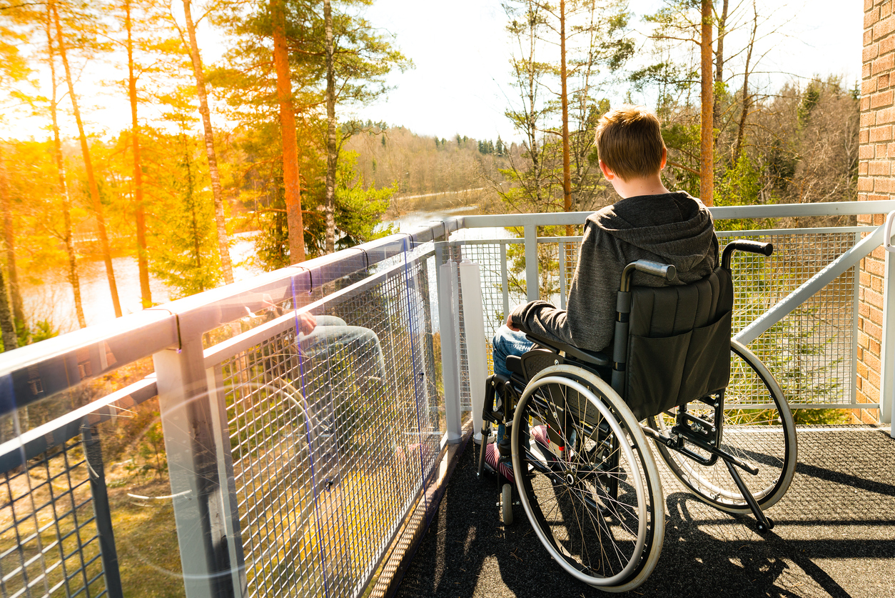 Young lonely man in a wheelchair on a balcony looking at the nature in the spring