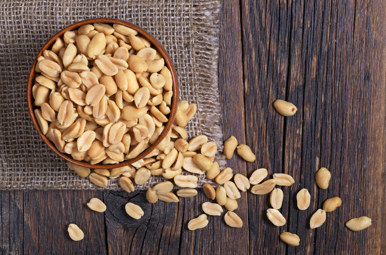Halves of roasted peanuts in bowl and near on dark wooden background, top view
