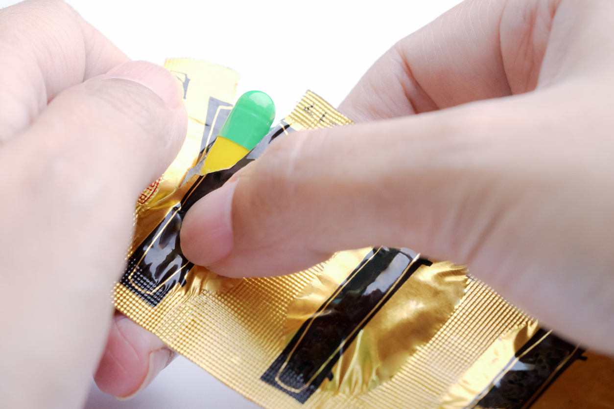 Hands tearing blister pack of green and yellow capsule, medical pill.