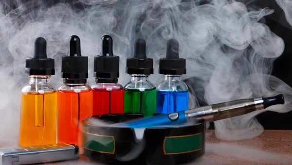Electronic cigarette on ashtray, cigarette lighter and bottles with vape liquid within vapor on black background