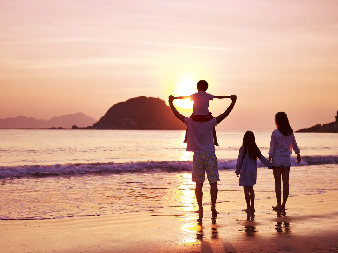asian family standing on beach watching and enjoying the sunrise.