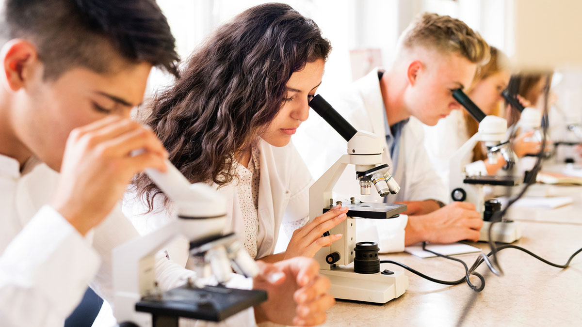 Beautiful high school students with microscopes in laboratory during biology class.