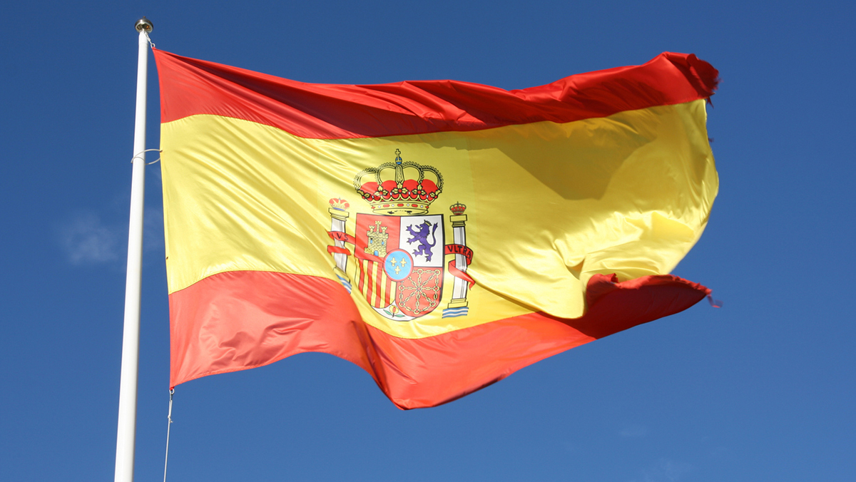 Flag of Spain waving in breeze with blue sky behind