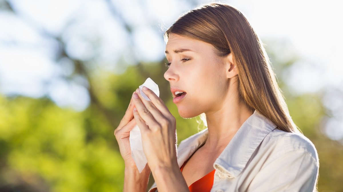 Beautiful woman using tissue while sneezing in park