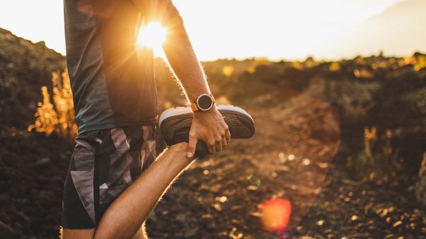 Male runner stretching leg and feet and preparing for running outdoors. Smart watch or fitness tracker on hand. Beautiful sun light on background. Active and healthy lifestyle concept.