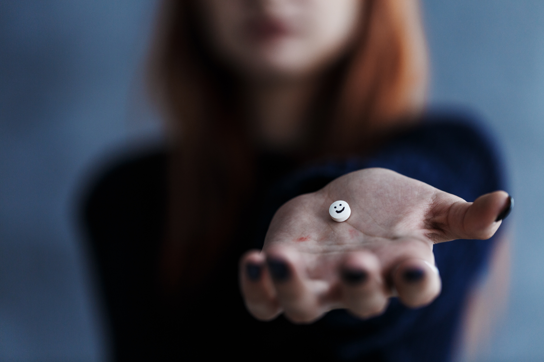 Close up of white pill with smiley face on a hand held by a young, ginger girl