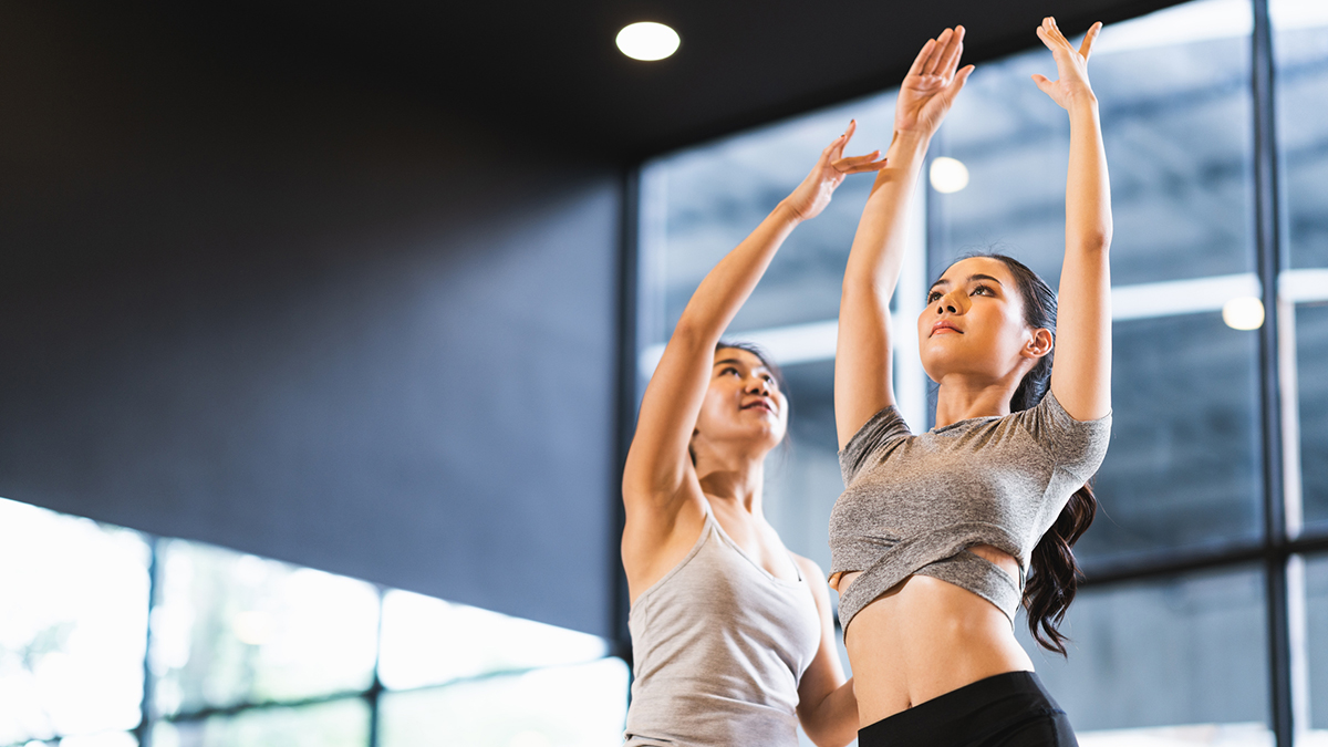 Beautiful Asian woman learning yoga pose with female instructor in yoga studio or health club. Sport exercise activity, gymnastics or ballet dancing class, or healthy people lifestyle concept