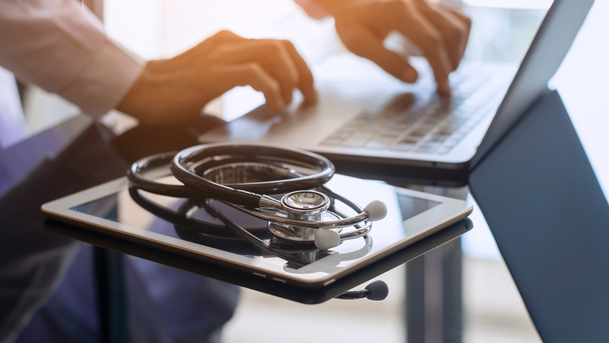 Male doctor hands typing on laptop computer keyboard, search medical information with digital tablet pc and medical stethoscope on the desk at office. Online medical,medic tech, emr, ehr concept.