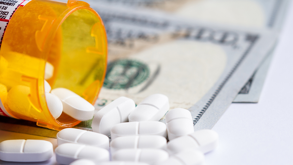 close up of a prescription bottle with white tables falling out on top of a group of hundred dollar bills